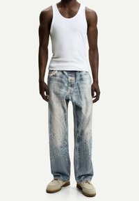 Bílý nátělník, roztrhané modré džíny s výřezy ve tvaru hvězd a viditelným šitím. Outfit doplňují béžové boty.