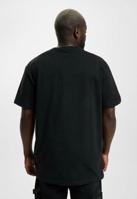 Black short-sleeve t-shirt with a relaxed fit, round neck, soft cotton texture, displayed from the back, showing an even hemline.
