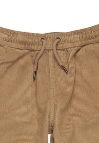 Pantalon en velours côtelé de couleur beige avec une texture côtelée. Taille élastique avec cordon de serrage et œillets en métal. Gros plan de la zone de taille.