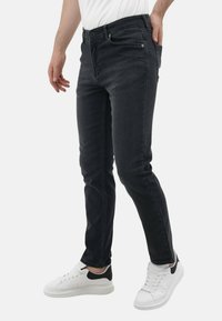 Zwarte denim jeans met een slim fit, voorzien van een klassieke vijf-pocket ontwerp en subtiele stiksels, gecombineerd met witte sneakers.