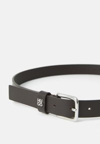 Ceinture en cuir brun avec une boucle en métal argenté, présentant un accent de logo sur une boucle en cuir. Texture lisse et design rectangulaire.