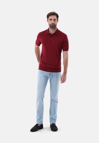 Burgunderfarbenes Polo-Shirt mit Kragen, kurzen Ärmeln und einer Drei-Knopf-Leiste, kombiniert mit hellblauen Jeans und schwarzen Slippern.