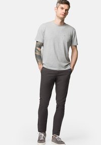 Szara koszulka z krótkim rękawem z kieszonką na piersi, w połączeniu z ciemnymi spodniami slim fit oraz szarymi trampkami, charakteryzująca się gładką fakturą i casualowym stylem.