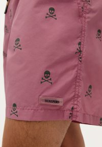 Shorts de baie roz, confecționați dintr-un material ușor, cu un model de oase și craniu de culoare neagră, având o etichetă cu logo-ul "SCALPERS" pe tiv.