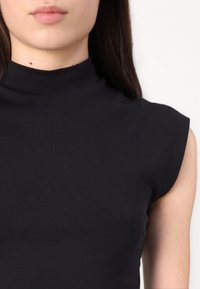 Haut sans manches noir à col montant en tissu doux. Présente un design ajusté avec une texture lisse et une silhouette simple.