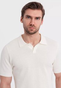 Bílá polokošile s krátkým rukávem, žebrovaným límcem, texturovaným materiálem a dvouknoflíkovým zapínáním. Padnoucí střih se subtilním pleteným vzorem.