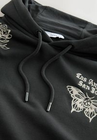 Donkergrijze hoodie met zwarte trekkoorden, voorzien van crèmekleurige borduursels van een roos en een vlinder met de tekst "Los Angeles San Jose".