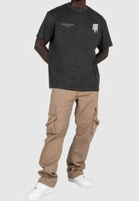 Camiseta de algodón de color gris oscuro con gráfico de texto, combinada con pantalones cargo color crema que tienen bolsillos laterales y un ajuste holgado. Zapatillas blancas completan el look.