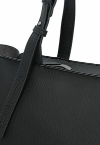 Sac à main en cuir noir avec une finition texturée, deux poignées et un logo de marque visible embossé sur la sangle. Pas de quincaillerie visible.