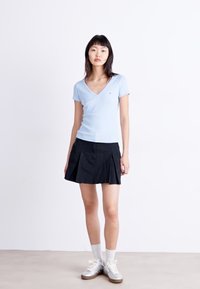 Lys blå, kortermet V-hals topp kombinert med en svart plisserte miniskjørt. Modellen har på seg hvite sokker og sølvfargede joggesko. Enkelt design.