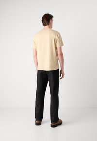 Beige bomulds t-shirt med rund hals, parret med mørke denim bukser. Sættet afsluttes med brune sko. Bagfra.