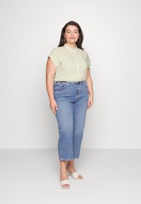 Camisa de manga corta con cuello, de rayas amarillas y blancas, combinada con unos jeans azules de tiro medio y sandalias de tacón abiertas color beige.