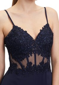 Robe bleu marine à fines bretelles avec dentelle florale complexe et perles sur un tulle transparent au niveau du corsage.