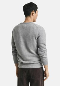 Maglione grigio lavorato a maglia con scollo rotondo e maniche lunghe. Presenta una consistenza sottile e polsi e orlo a coste. Viene mostrato il retro.
