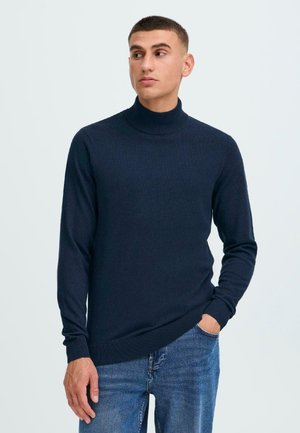 Marinefarbener Rollkragenpullover aus weichem Strickstoff, mit langen Ärmeln und gerippten Bündchen und Saum. Getragen mit blauen Jeans.
