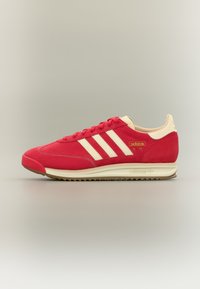 Adidași roșii Adidas SL 72 cu accente crem. Partea superioară din piele întoarsă, design cu trei dungi și talpă midsole albă. Talpă exterioară din cauciuc texturat.