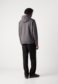 Felpa grigia con tasca a marsupio e cappuccio, indossata sopra dei pantaloni neri. Tessuto morbido, design aderente, con polsini e orlo a costine.