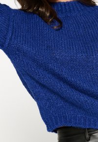 Pull en maille bleu profond, doté d'un col rond côtelé et d'une coupe ample. Tissu texturé avec une apparence légèrement épaisse.