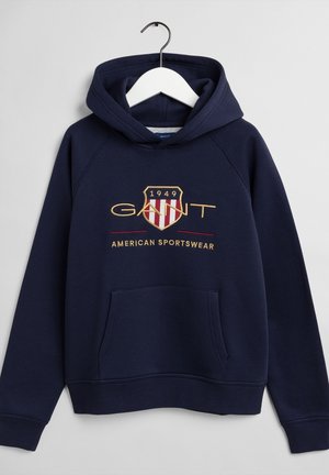 Sweat à capuche bleu marine avec poche avant, logo écusson brodé "GANT 1949" et texte "American Sportswear" sur la poitrine.
