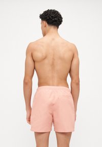 Roze kupaće kratke hlače s elastičnom waistbandom i detaljem zadnjeg džepa. Glatka tekstura i dužina do sredine bedara, pogodne za ležerne plažne kombinacije.
