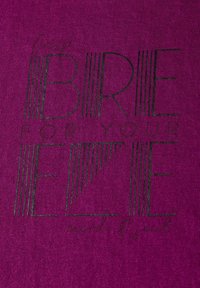 Tissu violet avec un motif tricoté texturé mettant en avant un texte imprimé noir : "BREEZE FOR YOUR EZE" avec un accent en cursive en dessous.