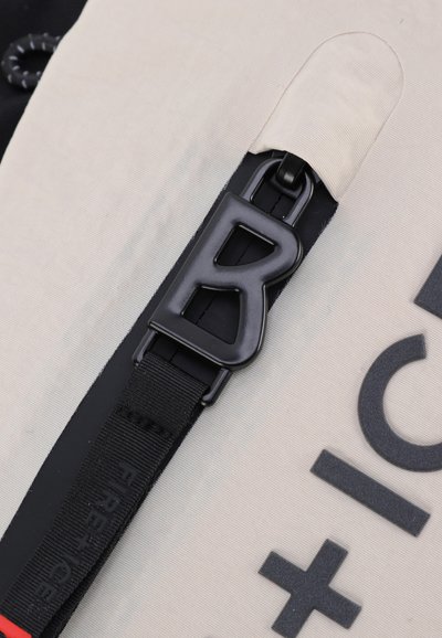 Tissu blanc avec des accents noirs présentant un clip en plastique noir proéminent étiqueté "B", accompagné de texte en relief et d'une sangle noire étiquetée "FIRE".