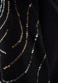Il tessuto nero presenta motivi vorticosi di piccole paillettes dorate e argentate, creando un design testurizzato e visivamente dinamico.