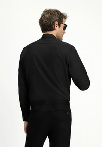 Camisa negra de manga larga con cuello clásico, textura suave y botones en los puños, combinada con pantalones negros con bolsillos traseros.
