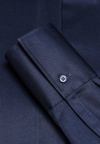 Donkerblauwe shirtmanchet met een gestructureerde afwerking, voorzien van een enkele knop en nette stiksels langs de randen.