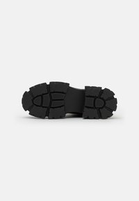 Suela de goma negra con patrones de banda de rodadura profundos, diseño plano y secciones texturizadas para un mejor agarre. Conexión suave con la entresuela.