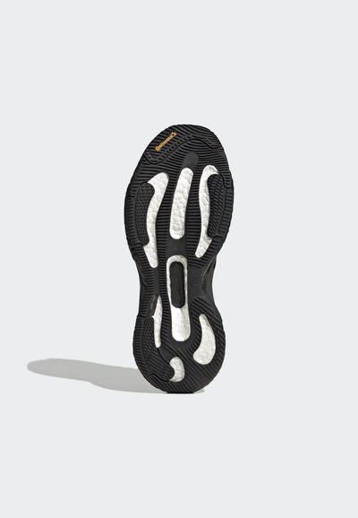 Semelle de sneaker en caoutchouc noir avec un profil texturé et des accents blancs, présentant un motif ondulé distinctif et des zones de rembourrage intégrées.