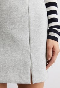 Hellgrau, Baumwollrock mit einem Schlitz vorne, glatter Textur und einem Saum, der direkt über dem Knie endet, kombiniert mit einem gestreiften Langarmshirt.