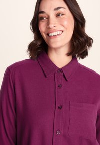 Purple button-up shirt made of textured fabric, featuring a collar, front pocket, and five matching buttons.