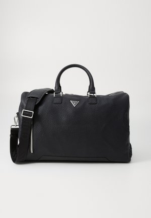 Black textured leather duffel bag with dual handles, detachable strap, silver hardware, and a metallic logo accent on the front.