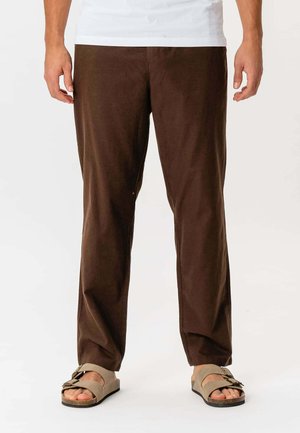 Brune bomuldsbukser med en afslappet pasform, der har en glat tekstur og et lige ben-design, parret med beige sandaler.