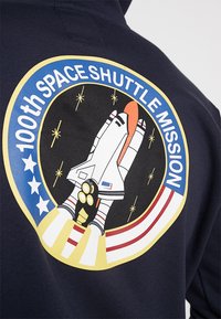 Sudadera bleumarin cu un grafic colorat al unei navete spațiale, textul "100th Space Shuttle Mission" și un fundal cu stele într-un design circular.