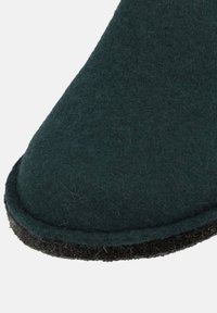 Dark green felt slipper with a rounded toe and black textured sole, featuring a durable stitching detail along the edge.