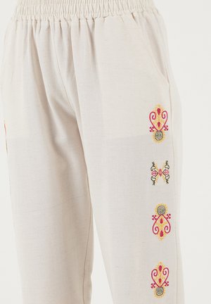 Bavlnené krémové nohavice s elastickým pásom. Majú farebnú kvetinovú výšivku pozdĺž bokov a bočné vrecká.