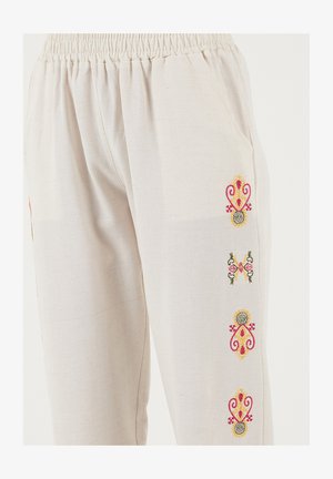 Kokvilnas krēmkrāsas bikses ar elastīgu vidukļa jostu. Tās rotā krāsaina ziedu izšuvumi gar sāniem un sānu kabatas.