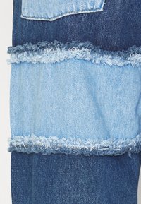 Tela de mezclilla azul con un diseño en capas y bordes deshilachados. Secciones alternas de azul claro y oscuro crean textura y contraste.