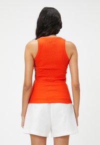 Top in cotone arancione a coste con un design aderente e scollatura rotonda. Abbinato a pantaloni corti bianchi, che mostrano una trama liscia e linee pulite.