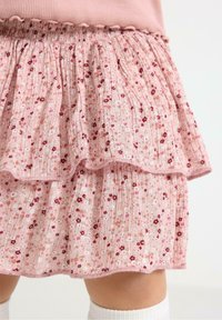 Gonna a balze con stampa floreale in morbido tessuto rosa pallido con bordi arricciati e vita elastica. Presenta piccoli fiori rossi e crema su tutto il capo.