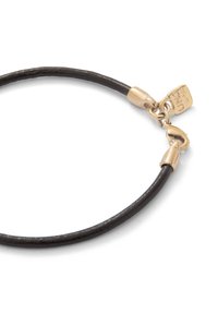 Pulsera de cuero negro con una textura suave, que presenta herrajes en tono dorado y una pequeña etiqueta. Diseño simple y flexible con cierre de clasp.