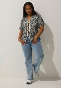 Svart blommig kortärmad blus med knyt framtill och vita accenter, ihop med ljusblå högmidjade jeans och vita sneakers.