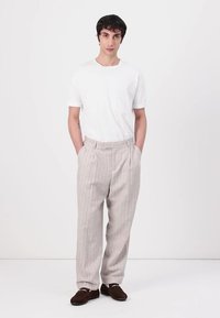 Lys grå pinstripede bukser med en afslappet pasform, ledsaget af en ensfarvet hvid t-shirt og mørkebrune slip-on sko.