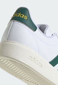 Biele kožené tenisky s zeleným akcentom na päte a bočnými pruhmi. Majú textúrovanú podrážku s drážkami a embosovaným logom značky.