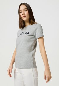 Camiseta de manga corta gris con la frase "PONY UP" en letras azul oscuro en el pecho. Tejido suave con diseño ajustado y aberturas laterales.