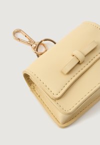 Portefeuille en cuir jaune avec rabat, orné d'un petit nœud en accent et d'un fermoir en métal doré. Bordures cousues et attache pour porte-clés.