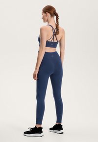 Námornícky športový podprsenka s prekríženými popruhmi v kombinácii s vysokými legínami. Mäkký, elastický materiál, doplnený čiernymi teniskami.