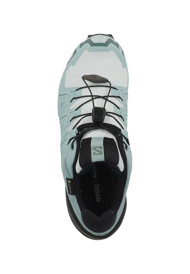 Chaussure de sport bleu clair et blanche avec une tige en mesh, un design asymétrique, un système de laçage rapide et une semelle noire. Présente la marque "Salomon".